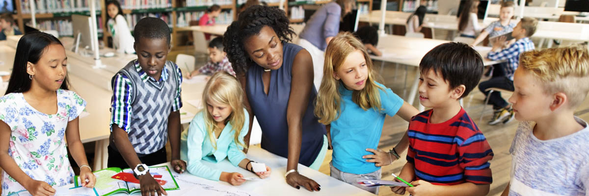 A teacher standing around a table wit her young students.