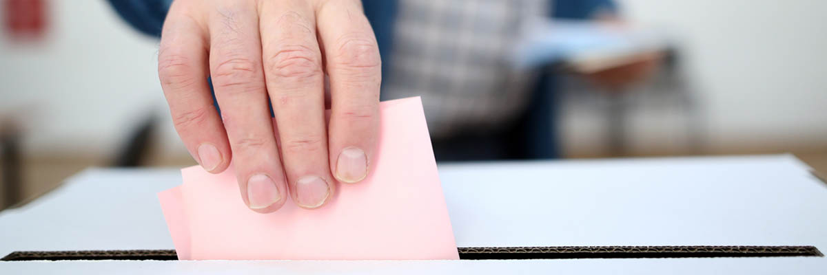 A hand placing a ballot in a box.